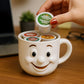 A person's hand is holding a coffee pod over a white mug with a smiling face, which is filled with coffee pods.