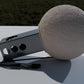 a large, round, white object resembling a ball or a sphere, placed on a white surface. There is a black wire or cable lying next to the object, and a small, rectangular object with three holes is also visible in the image.