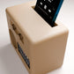 A beige-colored radio device is shown with a smartphone inserted into it, displaying a music player interface.