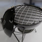 A black metal grill with a grid-like pattern on the grilling surface, placed on a stand.