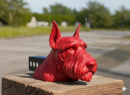 A red dog head sculpture is displayed on a wooden post, with a blurred background of trees and a road.