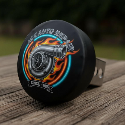 A close-up image of a black tire cover with a graphic design featuring a large engine and flames, along with the text "ACE AUTO REPAIR" and "SINCE 1985".