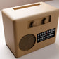 A tan-colored vintage radio with a speaker and two knobs, sitting on a white surface.