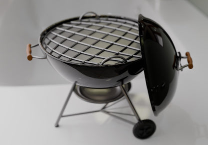 A small black grill with a metal grate and a wooden handle, placed on a white surface.