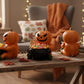 A Halloween-themed scene with three carved pumpkins sitting in black bowls, surrounded by candy and autumn leaves on a wooden table.