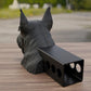 A black dog statue is sitting on a wooden surface, with a black rectangular object attached to its back.