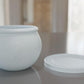 a white vase sitting on top of a table next to a white plate
