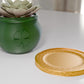 a green vase with a flower in it next to a gold plate