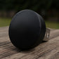 A black object is resting on a wooden surface, with a blurred background.