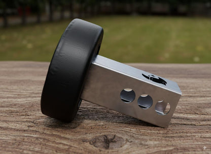 A black tire attached to a metal piece with holes on a wooden surface, with a blurred background of grass and trees.