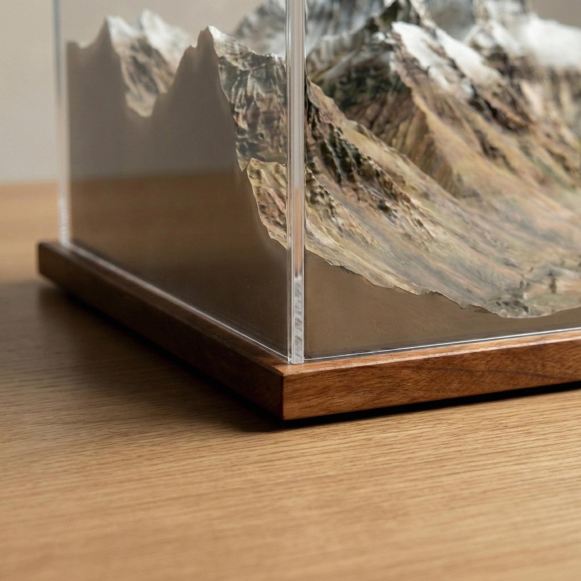 A close-up view of a wooden base and a glass display case containing a detailed model of a mountain landscape.