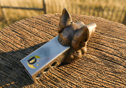 A bronze-colored metal object resembling a dog's head is resting on a wooden surface.