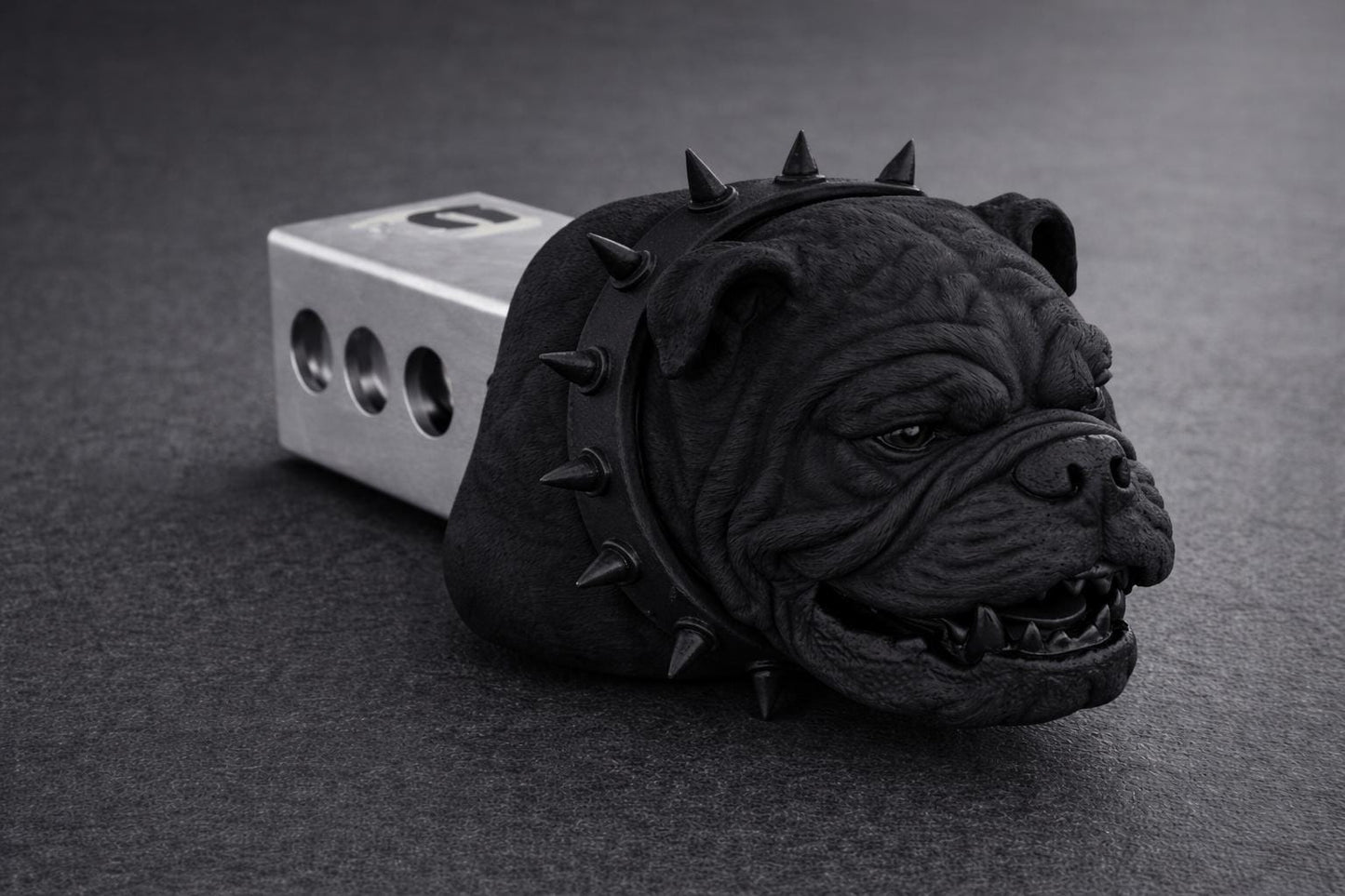 A black bulldog head with spikes is sitting on a gray surface.