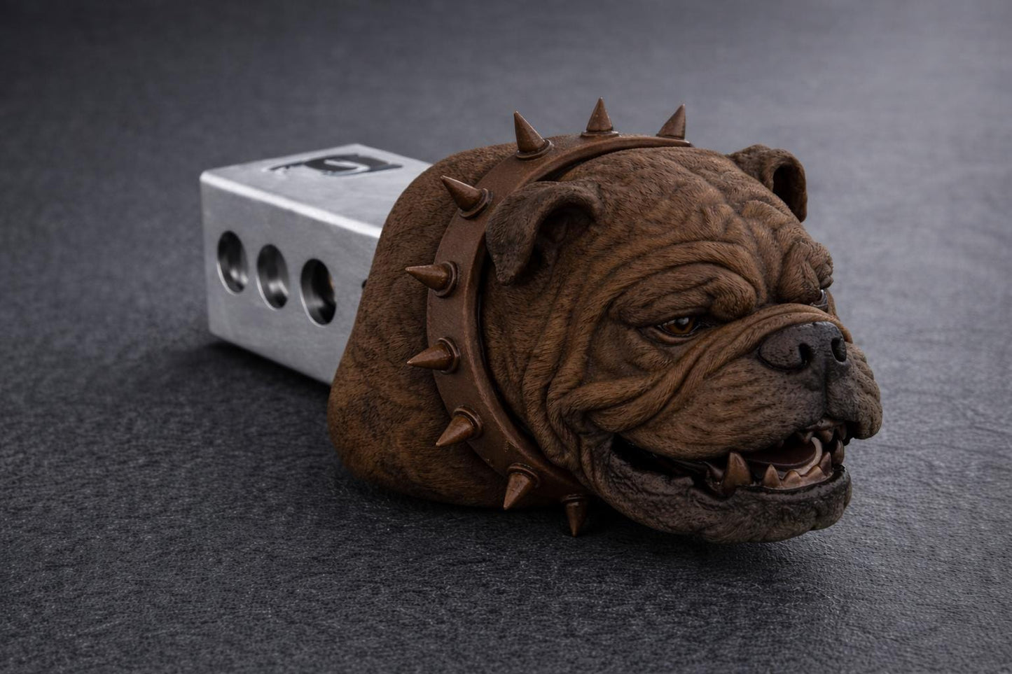 A brown bulldog head with spikes protruding from its mouth is resting on a gray surface.