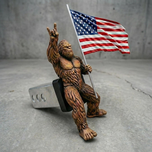 A brown, furry toy figure is holding up an American flag, standing on a gray surface.
