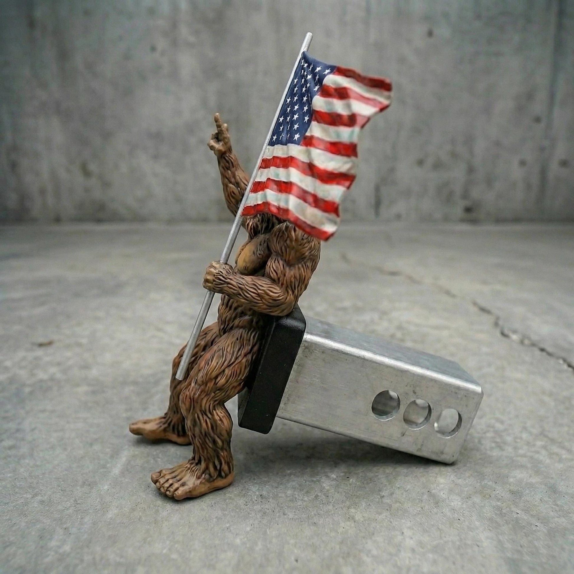 A brown bear figurine holding an American flag and sitting on a metal object.