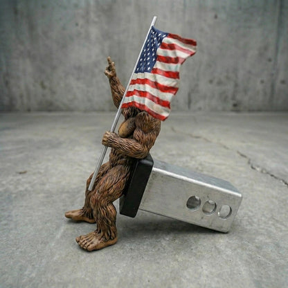 A brown bear figurine holding an American flag and sitting on a metal object.