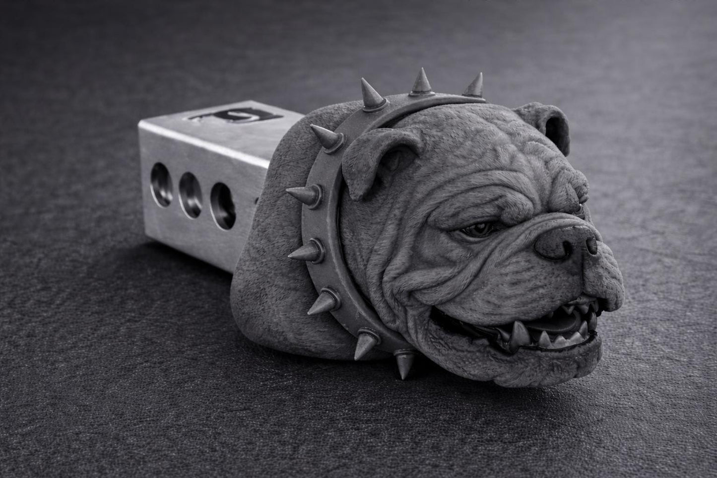 A close-up black and white image of a dog head with spikes on its collar, sitting on a dark surface.